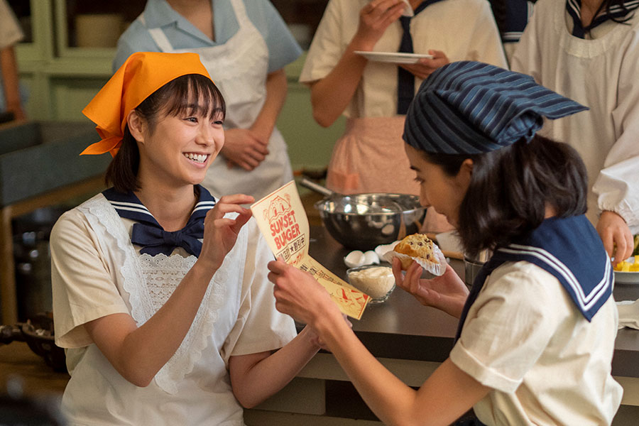 友人・前田早苗（左、高田夏帆）からハンバーガーショップの広告を渡される比嘉暢子（黒島結菜）(C)NHK