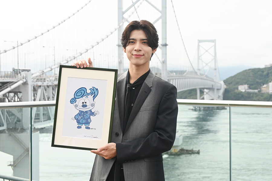 「うずしおビジョン」の除幕式に登壇したtimelesz・松島聡。鳴門海峡をバックに自身が手がけたキャラクター「淡路うず助」の原画と撮影(10月16日・道の駅うずしお)