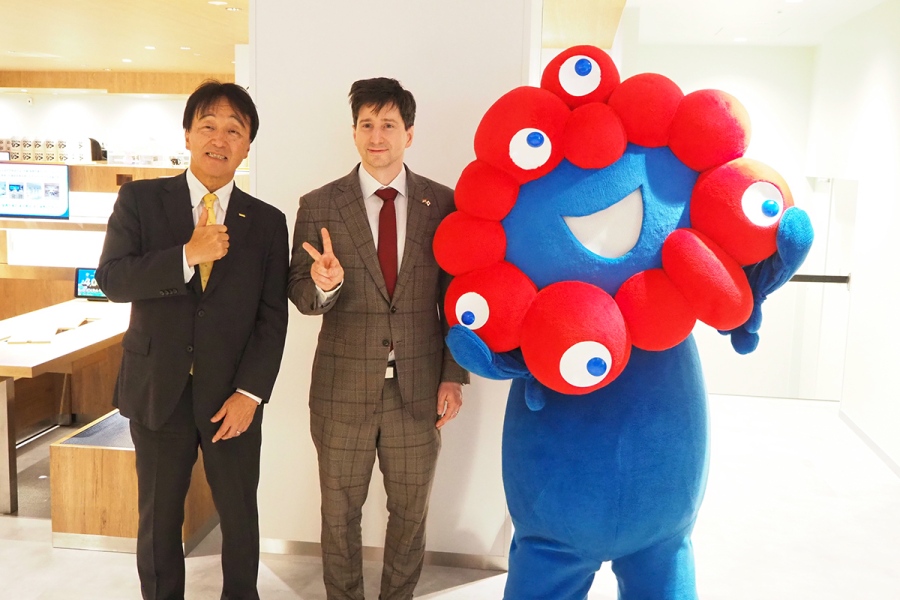 「くら寿司 メモリアル店 なんば千日前」内覧会にて、(左から)「くら寿司」取締役 広報・IR本部長の岡本浩之氏、在大阪ハンガリー領事館のケレケシュ・アンドラーシュ領事館長(万博店舗の世界のメニューではハンガリー料理が人気1位)、『大阪・関西万博』公式キャラクター・ミャクミャク(Lmaga.jp撮影)